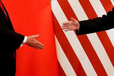 US China diplomats shake hands with each respective country flags in the background