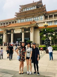 three girls posing in front of a traditional chinese gate to an institution