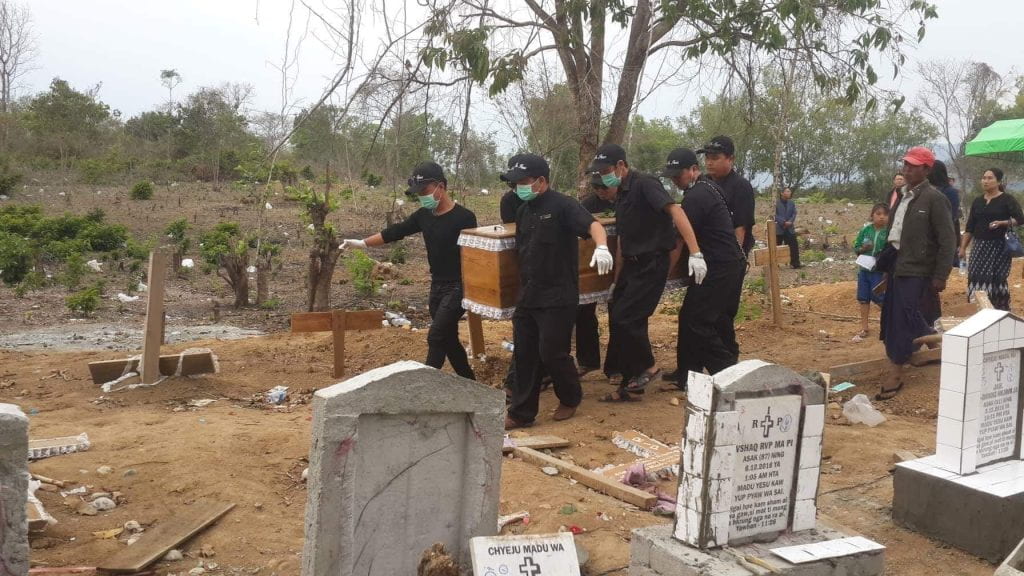 a team of people carrying a coffin to a burial plot at a local cemetery