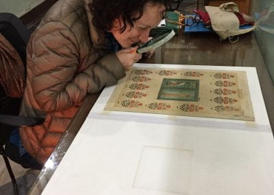 Mika Natif looking at tapestry Mughal painting through a magnifying glass