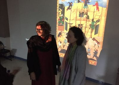 Kavita Singh and Mika Natif standing in front of a projector projecting photo of Mughal painting