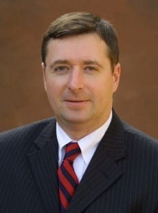 Headshot of Scott J White in professional attire and brown background