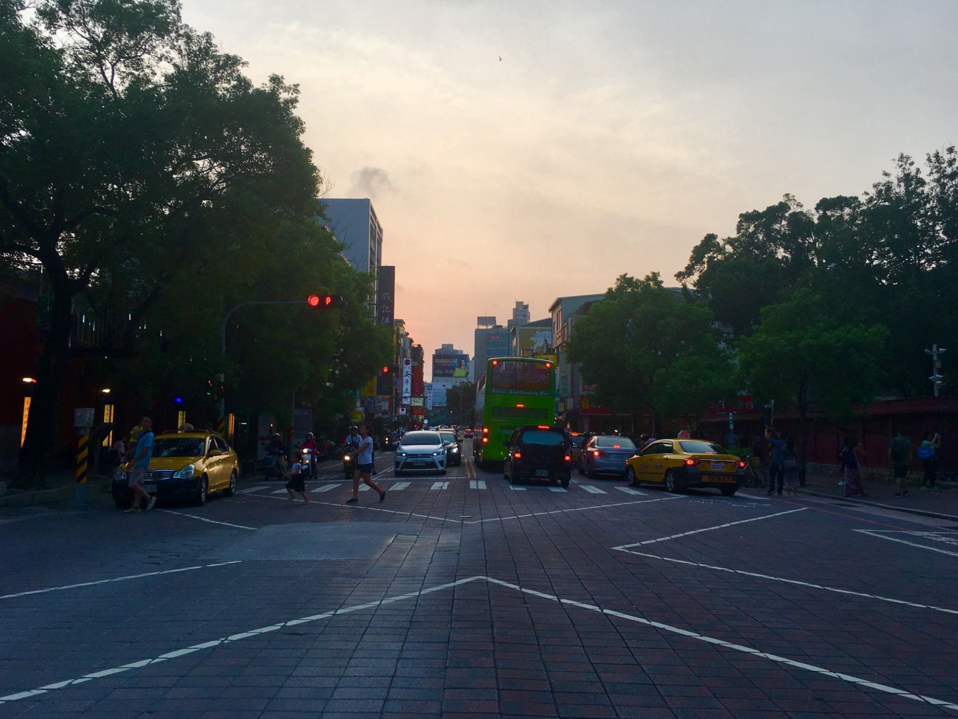A crowd crosses a busy intersection lined with cars in Tainan as the sun sets